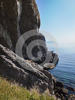 Steep cliff and huge stones on the shores of the blue water of the Black Sea. The coast of the village of Novy Svet in the Crimea.