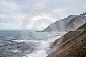 Steep cliffside with volcanic beach and waves crashing to shore. photo