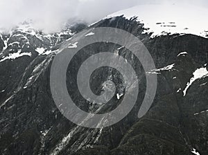 Steep Glacially Polished Cliffs And Mountain Peak Covered With Snow And Clouds, Alaska