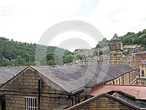 the steep hillside streets in hebden bridge between summer trees with the tower of the historic nutclough mill building