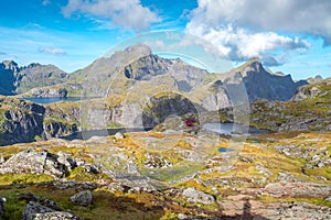 Steep mountains of Lofoten Island on a sunny arctic day. Hermannsdalstinden peak and red wooden cabin of Munkebu hut. Hiking