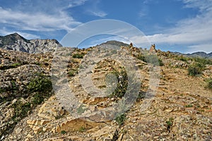 steep rocky mountainside with shrubs and views of the mountain range