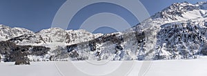Steep rocky slopes and Stampa village on frozen mountain lake, from Plaun da Lej, Switzerland