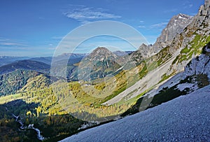 On a steep slope with a view of rocky mountains and green valleys with meadows and trees