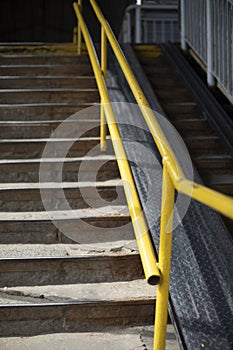 Steep stairs. Yellow handrail for climbing stairs. Overhead road crossing