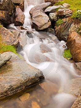 Steep stony stream bed of Alpine brook. Blurred waves of stream running over boulders and stones, high water level after rains