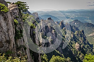 Steep vertical stone on the left leading to a valley and city in the far distance on the right in Huang Shan China