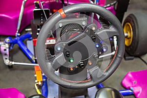 The steering wheel of the go-kart racing car is black with control buttons.