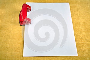 Stell hole puncher with blank sheet of paper, yellow background.