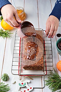 Step-by-step decoration of a carrot cake with chocolate glaze, ganache and candied fruits in a Christmas style on a light wooden