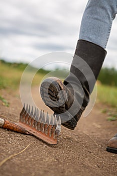 Step on the same rake. A man in kirza boots steps on a sharp metal rake.
