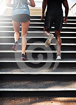 Step your game up. Rearview shot of two young people jogging up an outdoor flight of stairs.