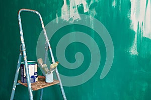 Stepladder, brushes and paint on the background of a green unpainted wall.