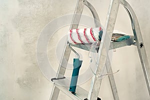 Stepladder, roller, brush on the background of a concrete wall. Construction and painting works