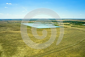 steppe rural landscape - sun-scorched grass, road, small lake and blue sky