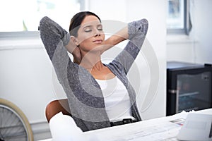 Stepping away for a moment. an attractive designer leaning back in her chair with her hands behind her head.