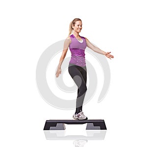 Stepping towards better fitness. A smiling young woman doing aerobics on an aerobic step against a white background.
