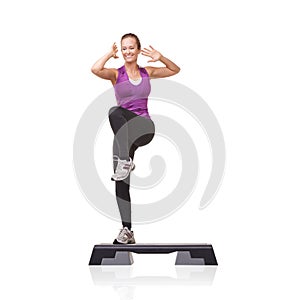 Stepping towards better health. A smiling young woman doing aerobics on an aerobic step against a white background.