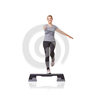 Stepping towards her fitness goals. A smiling young woman doing aerobics on an aerobics step against a white background.