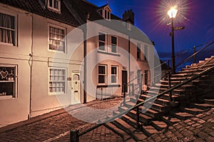 Steps and cottages illuminated by a street lamp at dusk.