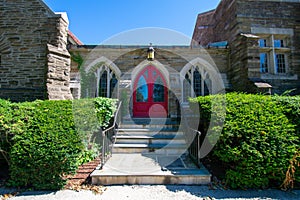 Steps Leading Up to the Red Door of a Cobblestone Church With Trimmed Bushes on Each Side