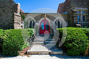 Steps Leading Up to the Red Door of a Cobblestone Church With Trimmed Bushes on Each Side