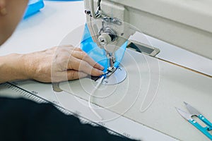Stepwise stitching of blue fabric medical masks on a sewing machine. A close up of an industrial sewing machine makes a seam. The photo