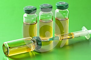 Sterile medical vials with medication solution, ampoules, and syringe on a light green background
