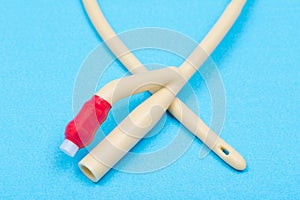 Sterile silicone-elastomer coated latex Foley urinary catheter  with balloon port and drainage port isolated on blue background