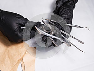 Sterilized manicure items in kraft paper packaging. Hands in black surgical protective gloves hold manicure devices.