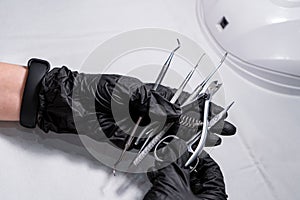 Sterilized manicure items in kraft paper packaging. Hands in black surgical protective gloves hold manicure devices.