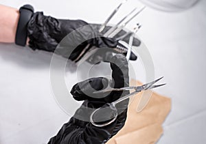 Sterilized manicure items in kraft paper packaging. Hands in black surgical protective gloves hold manicure devices.