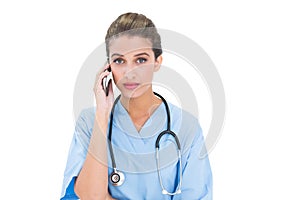 Stern brown haired nurse in blue scrubs making a phone call