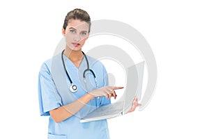 Stern brown haired nurse in blue scrubs using a laptop