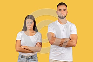 Stern-faced young couple with arms crossed in white t-shirts, exuding a strong sense of disagreement