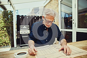 Stern senior man reading a financial newspaper at home