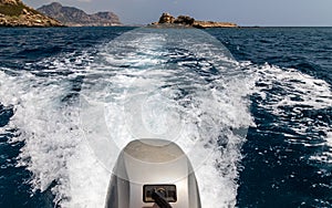 Stern wave of a motor boat with the motor in foreground and the rocky coastline on the eastside of Greek island Rhodes in the