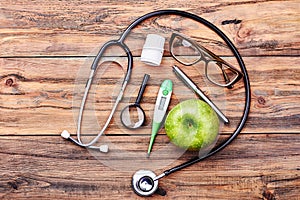 Stethoscope, apple, thermometer and loupe.