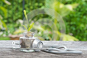 Stethoscope on bottle, coin and plant on wooden background. Concept of financial planning for health care.