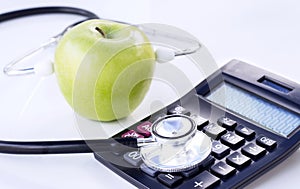 Stethoscope, calculator and green apple isolated on white table