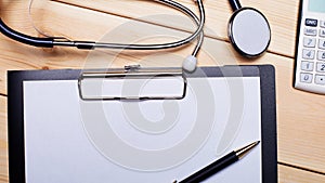 Stethoscope, calculator, sheet of paper and pen lie on a wooden background. Copy space. Flat lay. Medical concept