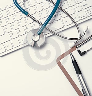 Stethoscope on computer keyboard on white background. Physician write medical case long term care treatment concept, top view,