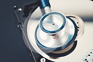 Stethoscope on dusty dismantle hard disk over dark background