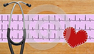 stethoscope, electrocardiogram graph (ECG) and textile heart over wooden background