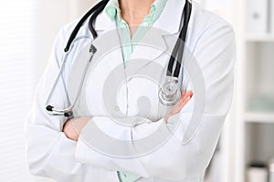 Stethoscope at female doctor breast at hospital office. Unknown physician`s hands close-up. Green tone of blouse