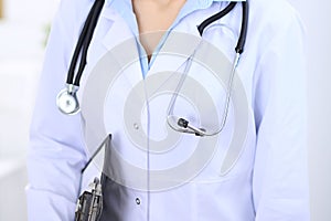 Stethoscope at female doctor breast at hospital office. Unknown physician`s hands close-up. Medicine and health care
