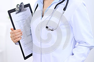 Stethoscope at female doctor breast at hospital office. Unknown physician`s hands close-up. Medicine and health care