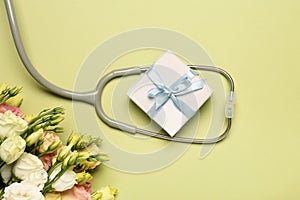 Stethoscope, gift box and eustoma flowers on light green background, flat lay. Happy Doctor\'s Day