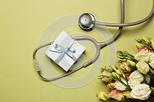 Stethoscope, gift box and eustoma flowers on light green background, flat lay. Happy Doctor\'s Day