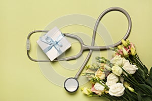 Stethoscope, gift box and eustoma flowers on light green background, flat lay. Happy Doctor\'s Day